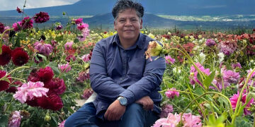 Alejandro Lira sentado entre flores, con montañas al fondo.