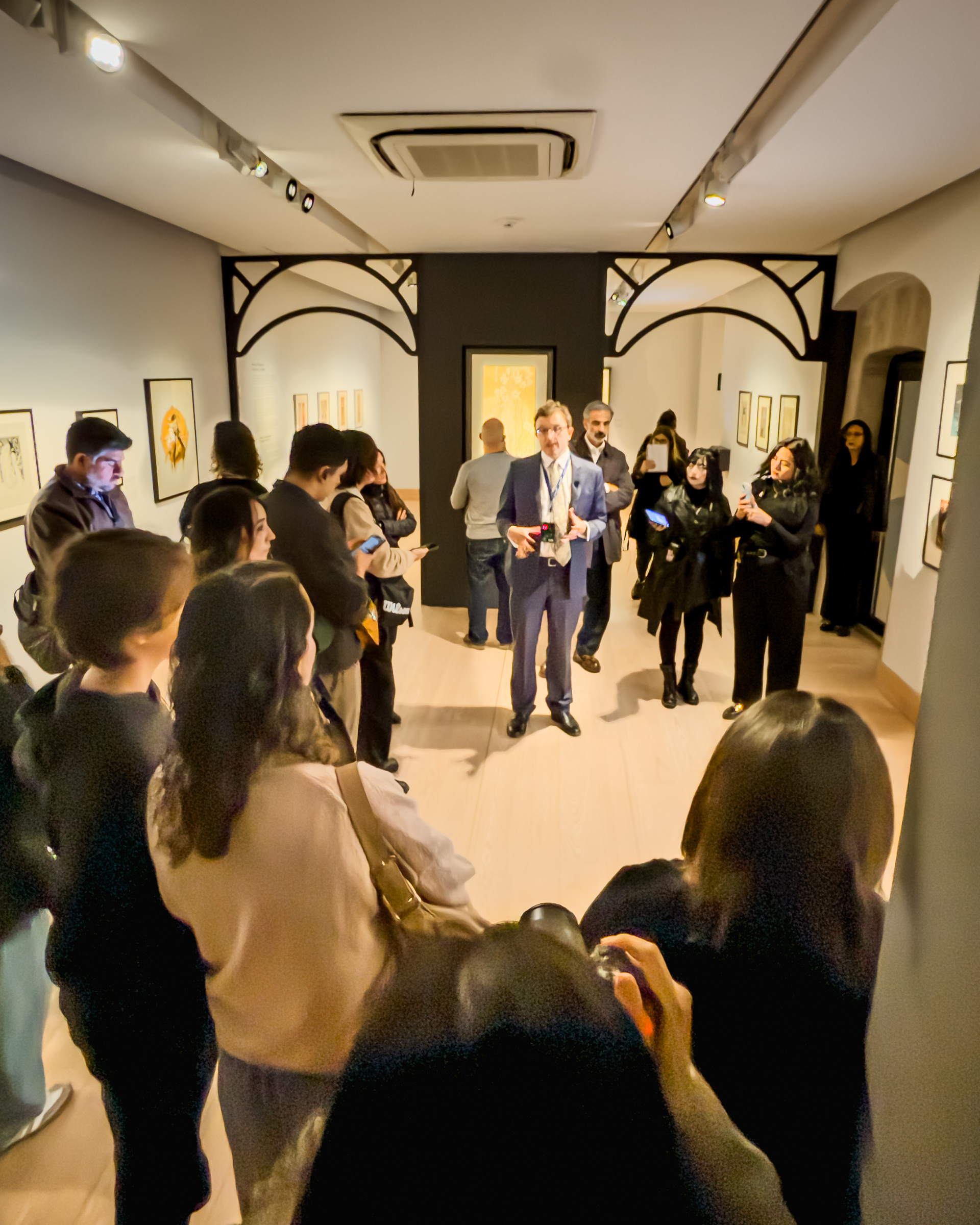Asistentes en una sala de la exposición de Alphonse Mucha, con estructuras decorativas de líneas curvas.