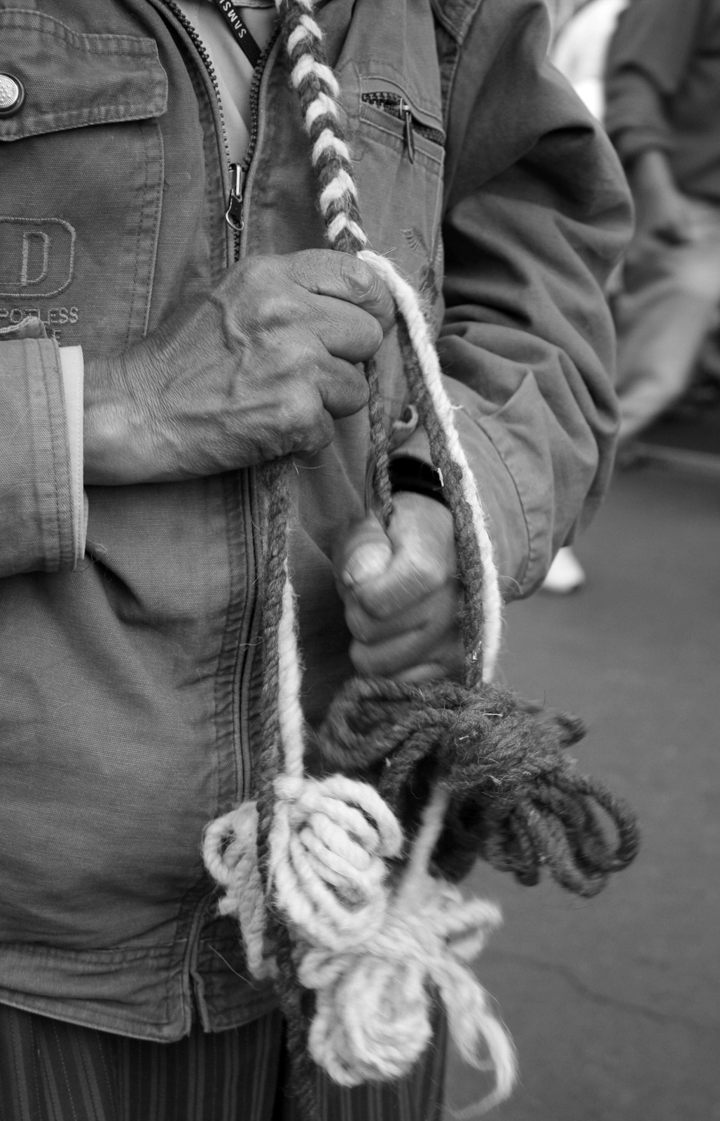 Manos trabajando una trenza de fibras claras y oscuras con manojos de hebras en los extremos.